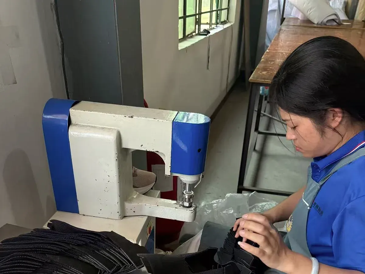 GRAND STAR employee handling dark footwear components beside production equipment